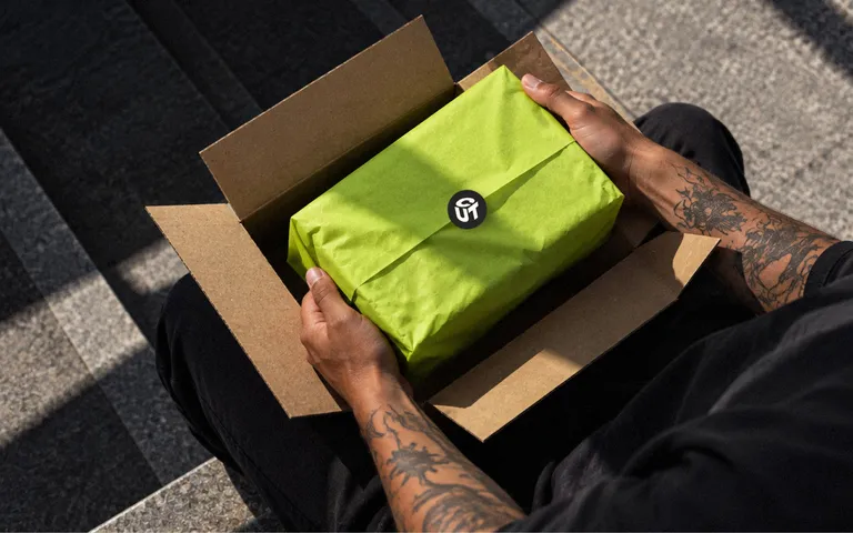 Hands opening a kraft box with a lime-wrapped parcel sealed with the Cut Form monogram