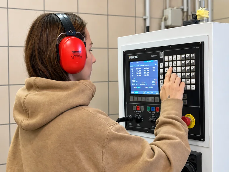 Alisa in red ear defenders setting up the CNC router at its control panel