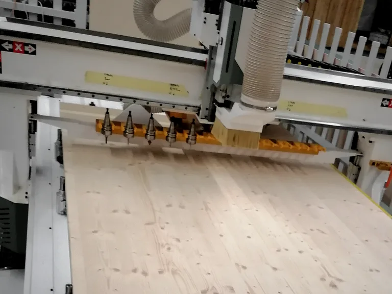 Our CNC machine: the gantry with its dust hood above a spruce panel, the tool rack with cutters along the side